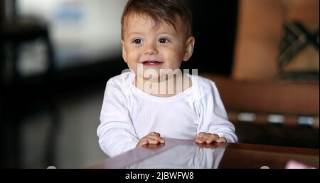 Adorable bébé se cachant sous la table. Bébé garçon souriant à l'appareil photo portrait jouant peekaboo Banque D'Images