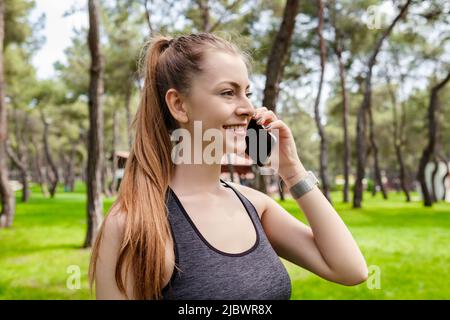 Jeune femme brune portant des vêtements de sport sur le parc de la ville, parlant à l'extérieur sur un téléphone portable avec des amis ou un petit ami avec le sourire. Banque D'Images