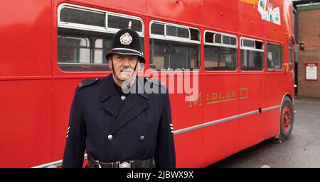 un policier britannique vintage se tenant devant un bus rouge à impériale Banque D'Images