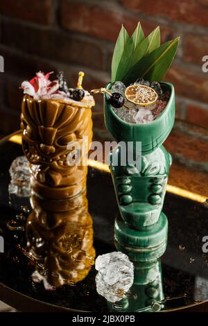 Cocktails Tiki. Deux cocktails dans des verres différents sur le fond d'un bar décoré de fruits secs et de feuilles tropicales Banque D'Images