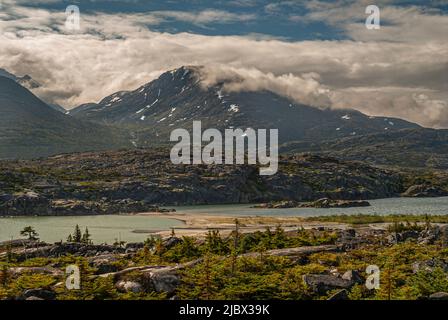 Skagway, Alaska, États-Unis - 20 juillet 2011 : route du Klondike vers le Canada. Le banc de sable divise le lac d'été. Cloudscape au-dessus des Rocheuses canadiennes avec des patchs de neige et Banque D'Images