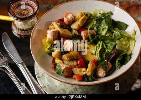 Une salade avec du saumon grillé, une purée d'avocat et de la laitue garnie de fromage à la crème. Gros plan du plat dans un bol marron isolé sur fond marron Banque D'Images