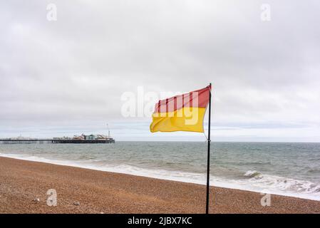 Sauveteurs rouges et jaunes sur le drapeau de service à la plage de Brighton avec le Brighton Pier en arrière-plan, un jour couvert, East Sussex, Angleterre, Royaume-Uni Banque D'Images