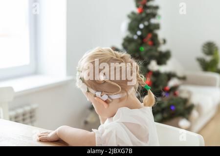 Enfant fille vêtue d'une robe de noël avec implants cochléaires s'amusant à la maison - diversité et aide auditive et technologies innovantes pour le traitement Banque D'Images