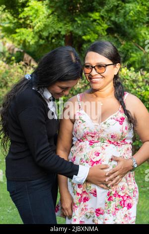 La fille latine tient les mains de sa mère sur son ventre enceinte. Banque D'Images