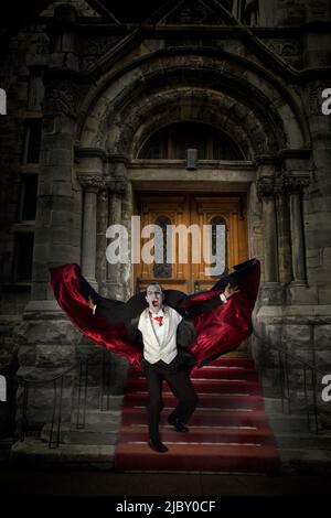 Compter Dracula montrant des fangs et tenant son cap dehors tout en courant vers la caméra en bas des escaliers du bâtiment en pierre Banque D'Images