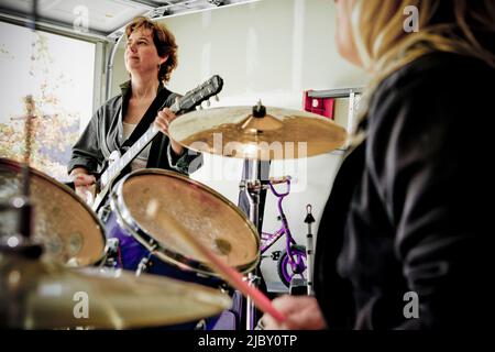 Vue sur les tambours épaule de joueur de guitare dans le groupe de garage composé de femmes d'âge moyen, pratiquant dans le garage résidentiel Banque D'Images