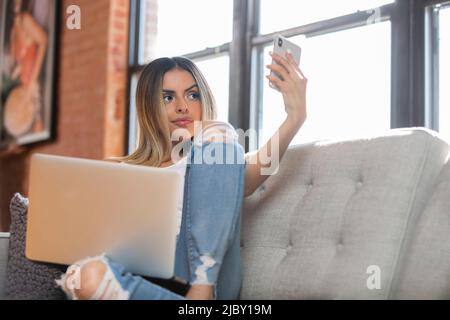 Une jeune femme hispanique prend le selfie par téléphone portable tout en étant assise sur un canapé à la maison Banque D'Images