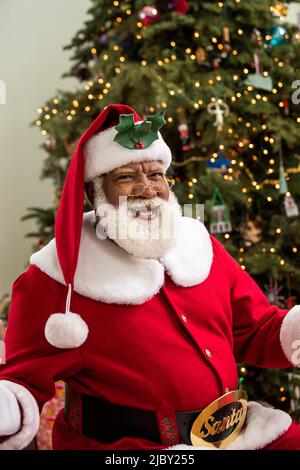 Homme âgé habillé comme Père Noël Noir avec ses bras ouverts vers l'appareil photo souriant. Banque D'Images