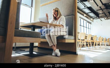 Entrepreneur mature ayant une réunion virtuelle dans un espace de travail moderne. Bonne femme d'affaires mûre souriant gaiement pendant un appel vidéo. Bus expérimenté Banque D'Images