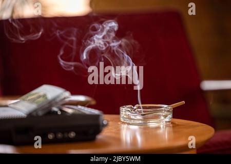 Partie antérieure, détail de la table latérale avec magnétophone / répondeur et cendrier rétro doté d'un joint de pré-roulis CBD éclairé, cigarette avec fumée montante Banque D'Images