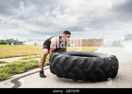 Un hispanique musclé portant un débardeur avec un tatouage « fort » sur son biceps, qui fait basculer le pneu du tracteur Banque D'Images