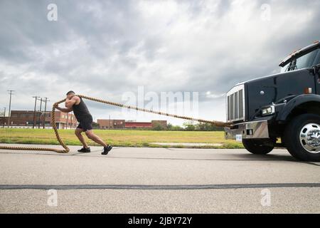 Homme hispanique musclé portant le haut de réservoir, tirant semi-camion avec grande corde de remorquage Banque D'Images