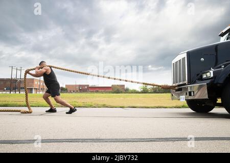 Homme hispanique musclé portant le haut de réservoir, tirant semi-camion avec grande corde de remorquage Banque D'Images