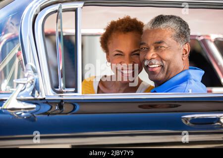 Un couple plus âgé assis dans une voiture classique qui cherche un appareil photo souriant Banque D'Images