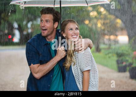 Jeune couple marchant dans le parc avec un parapluie sous la pluie, tous deux regardant la pluie qui tombe Banque D'Images