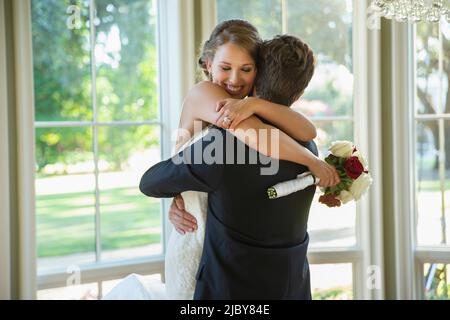 Mariée et marié dans une étreinte, marié levant la mariée debout par une grande banque de fenêtres Banque D'Images