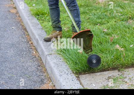 Travailleur dans une tondeuse à essence en main, homme tond l'herbe avec un coupe-ficelle Banque D'Images