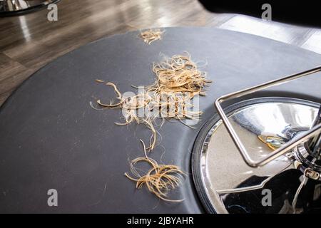 Détail des cheveux coupés sur le sol sous la chaise au salon de coiffure boutique Banque D'Images