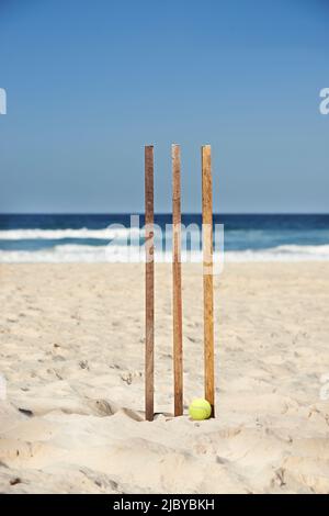 Casquette avec drapeau australien reposant sur des souches de cricket en bois et ballon de tennis à la plage