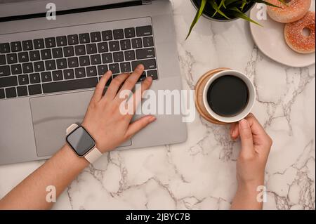 Une femme d'affaires travaillant à son bureau, utilisant un ordinateur portable tout en sirotant un café du matin. Espace de travail avec concept d'arrière-plan en marbre, t Banque D'Images