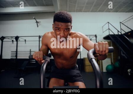 Afro-américain utilisant un entraîneur elliptique pendant l'entraînement de cross-fit. Athlète masculin s'exerçant intensément dans la salle de sport. Photo de haute qualité Banque D'Images