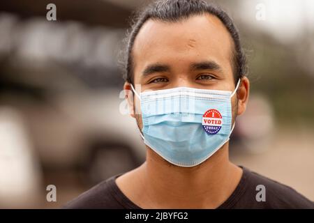 Un homme hispanique portant un masque et un autocollant J'ai voté aujourd'hui sur le masque regardant directement dans l'appareil photo Banque D'Images