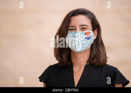 Femme caucasienne portant un masque et un autocollant J'ai voté aujourd'hui sur le masque, regardant dans l'appareil-photo souriant. Banque D'Images