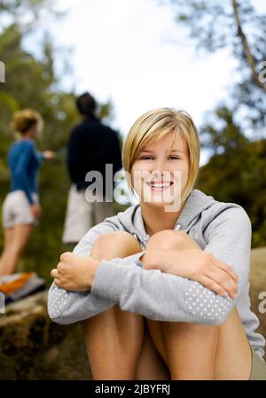 Portrait d'une jeune femme assise sur un rocher souriant et couple derrière appréciant les environs dans le désert Banque D'Images