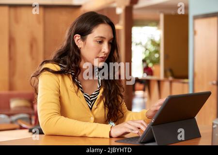 Portrait d'une jeune femme ethnique portant un chandail jaune avec un chemisier rayé noir et blanc, assis au bar dans la cuisine du centre-ville loft avec iPad Banque D'Images