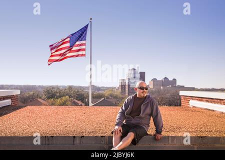 Smiling man sitting on toit près de drapeau américain Banque D'Images