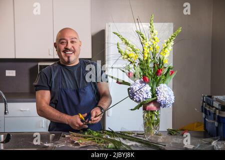 Smiling man arranging flowers in kitchen Banque D'Images