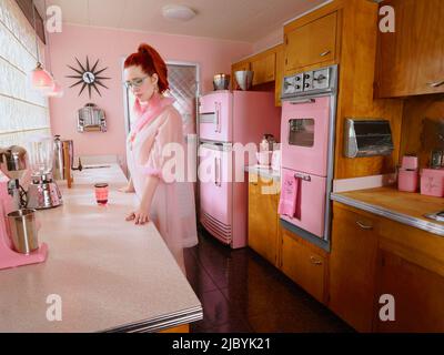 Portrait vintage de femme perdue dans la pensée dans une cuisine de style du milieu du siècle. Banque D'Images