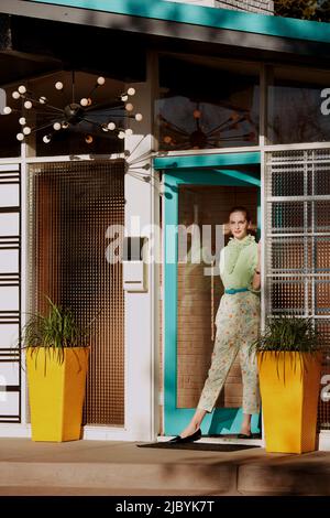 Portrait contemporain sur le thème vintage d'une femme debout dans une porte d'entrée d'une maison de style du milieu du siècle. Banque D'Images