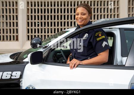 Policier debout à la porte de la voiture de police regardant vers la caméra souriante Banque D'Images