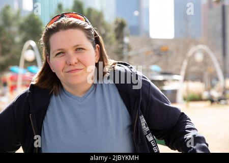 Portrait d'une femme d'âge moyen assise dans un parc portant un sweat à capuche et des lunettes de soleil sur la tête, souriant en regardant l'appareil photo Banque D'Images