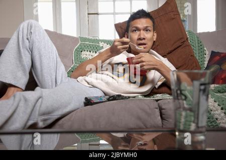 Lazy Man eating sur canapé et regarder la télévision Banque D'Images