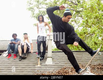 Des amis qui regardent un homme skate sur le toit Banque D'Images