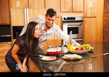 Femme soufflant des bougies d'anniversaire dans la cuisine Banque D'Images