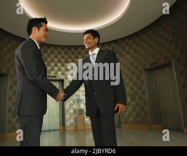 Businessmen shaking hands in office lobby Banque D'Images