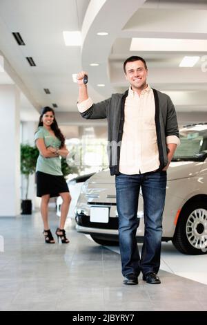 L'homme orgueilleux holding keys to new car in showroom Banque D'Images