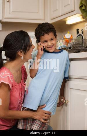 Hispanic mother helping son talk on cell phone Banque D'Images