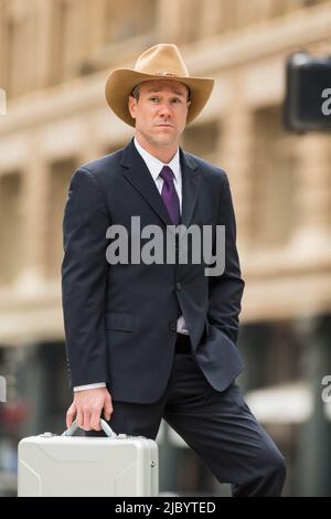 Man in cowboy hat carrying briefcase on city street Banque D'Images
