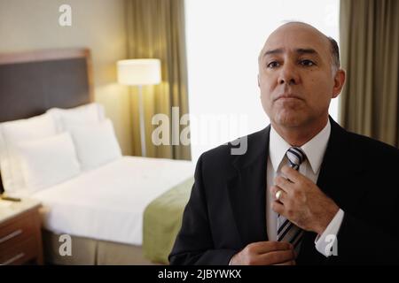 Middle-aged businessman adjusting tie in hotel room Banque D'Images