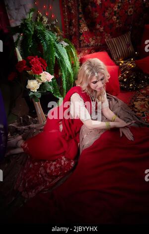 Une belle fille européenne qui ressemble à une femme arabe dans une pièce rouge dans un harem. Photo d'un style oriental odalisque. Un modèle pose dans un sari AS Banque D'Images