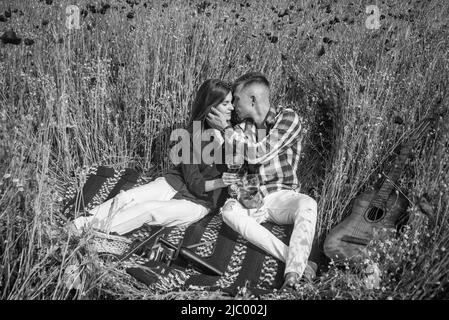 les amateurs de guitare boivent du vin dans le champ de fleurs. musique. couple amoureux. homme et femme dans le champ de pavot. Banque D'Images