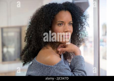 Une femme d'âge moyen regarde une fenêtre avec sa main sous son menton. Banque D'Images