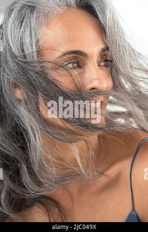 Une jeune femme d'âge moyen regarde vers la droite quand le vent souffle ses cheveux gris sur son visage. Banque D'Images