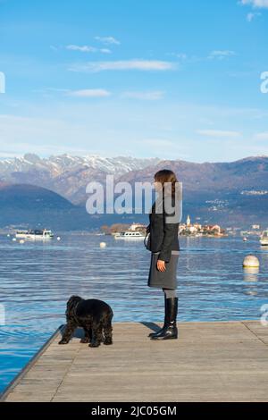 Femme élégante debout sur un quai avec son chien à Stresa, Piémont, Italie. Banque D'Images