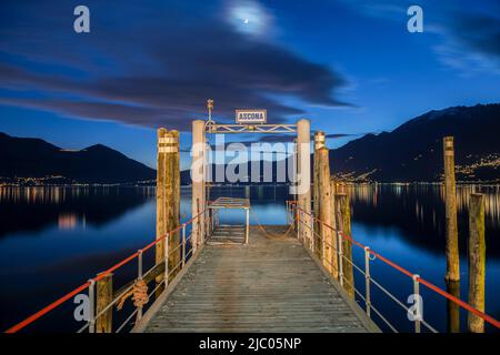 Jetée sur le lac alpin majeur avec lumière de montagne et de lune à Dusk à Ascona, Suisse. Banque D'Images